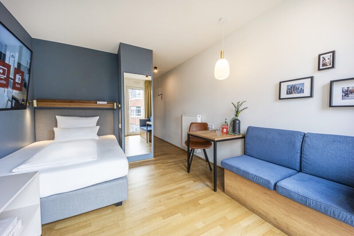 Ein modernes Hotelzimmer mit einem Bett, einer Couch, einem Tisch mit Stuhl und einer Pendelleuchte.