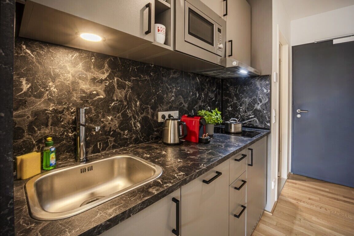 A modern kitchen with a marble countertop, stainless steel sink, and built-in appliances.