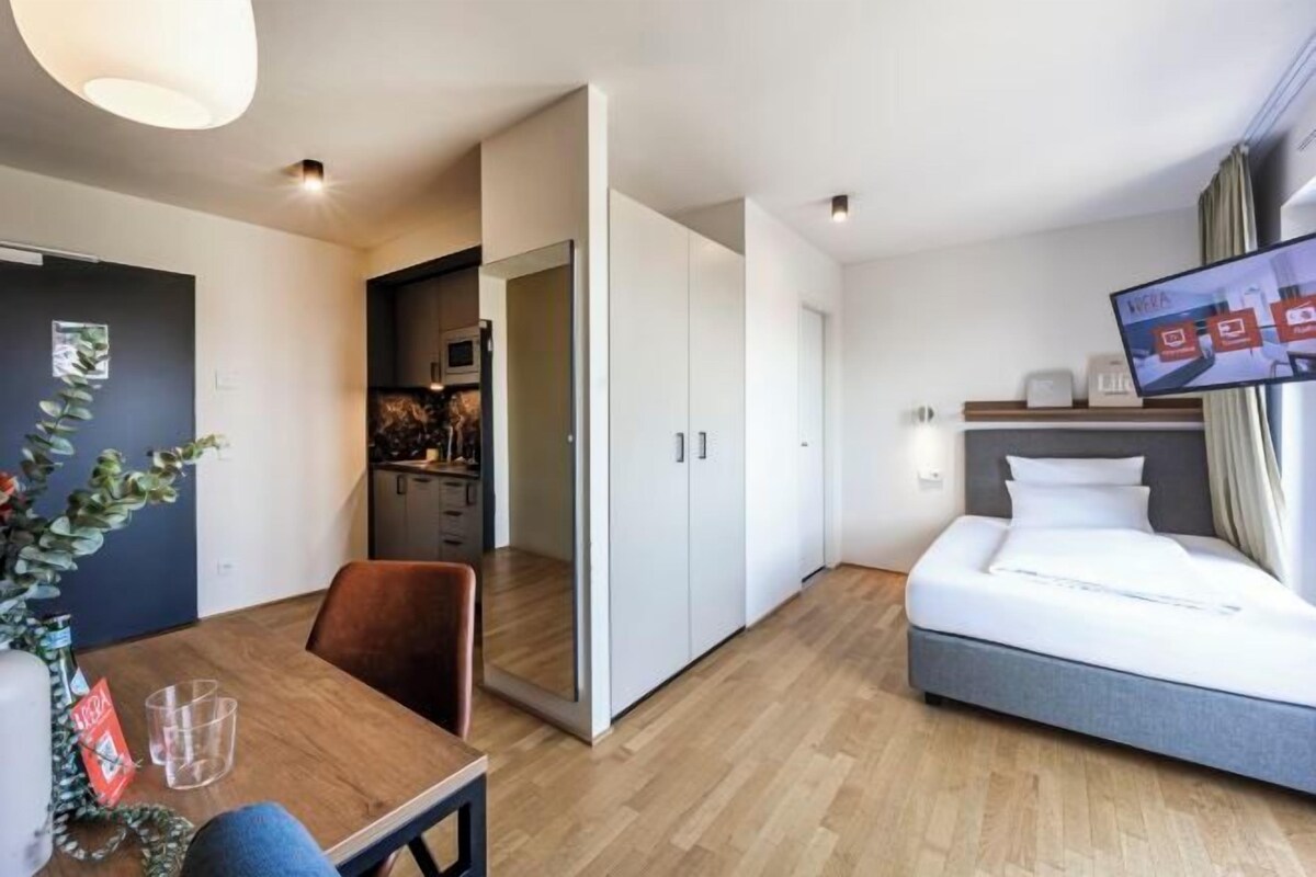 Una habitación de hotel con cama, televisión, mesa de comedor y zona de cocina.