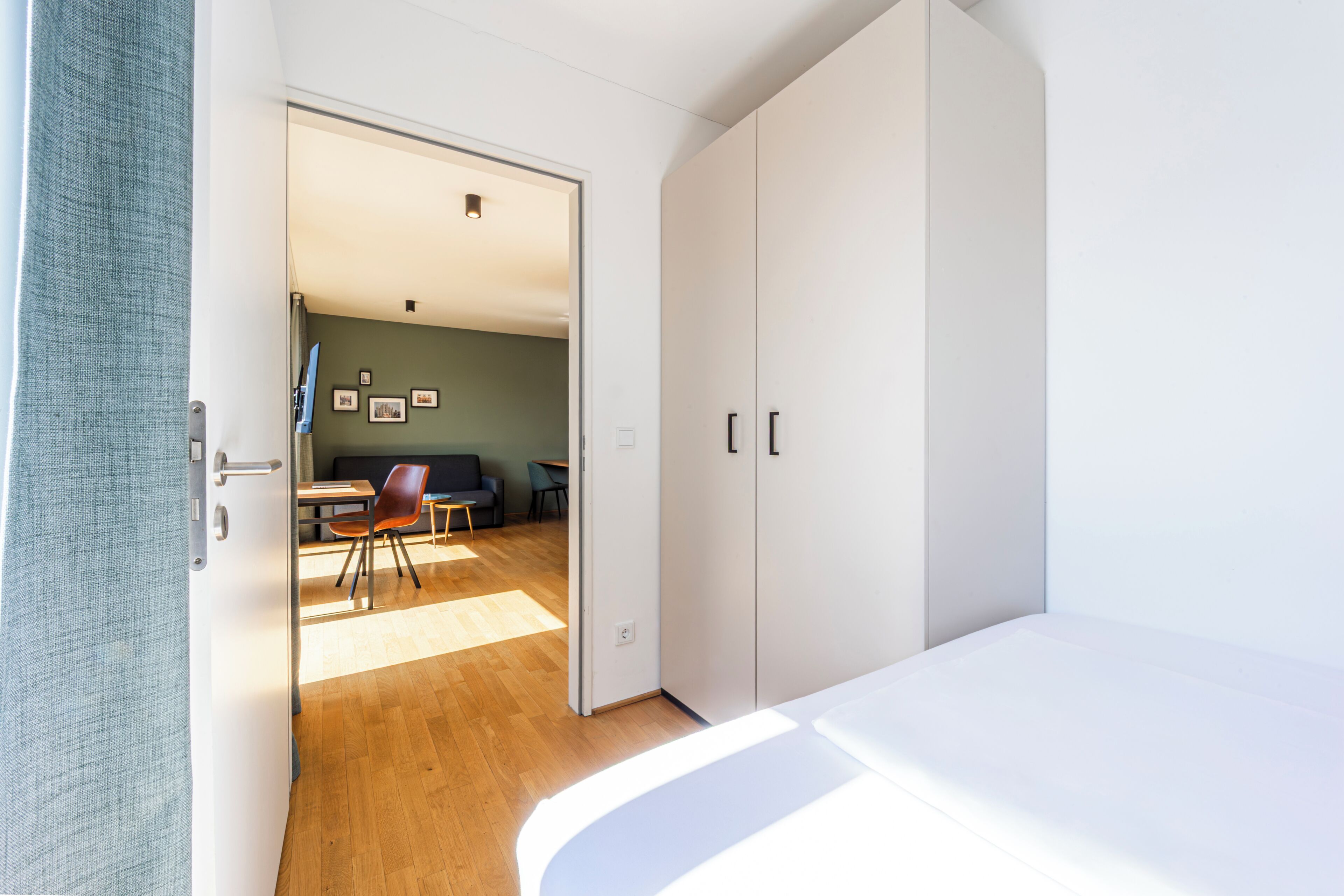 Une chambre à coucher comprenant un lit, une armoire et une porte donnant sur un espace de vie avec un canapé et une table.