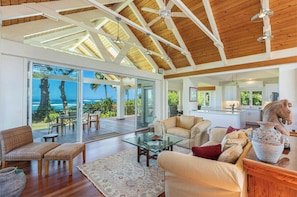 Relax in this spacious living area with a high ceiling, featuring a sofa, coffee table, and wicker chair, and take in the ocean view.