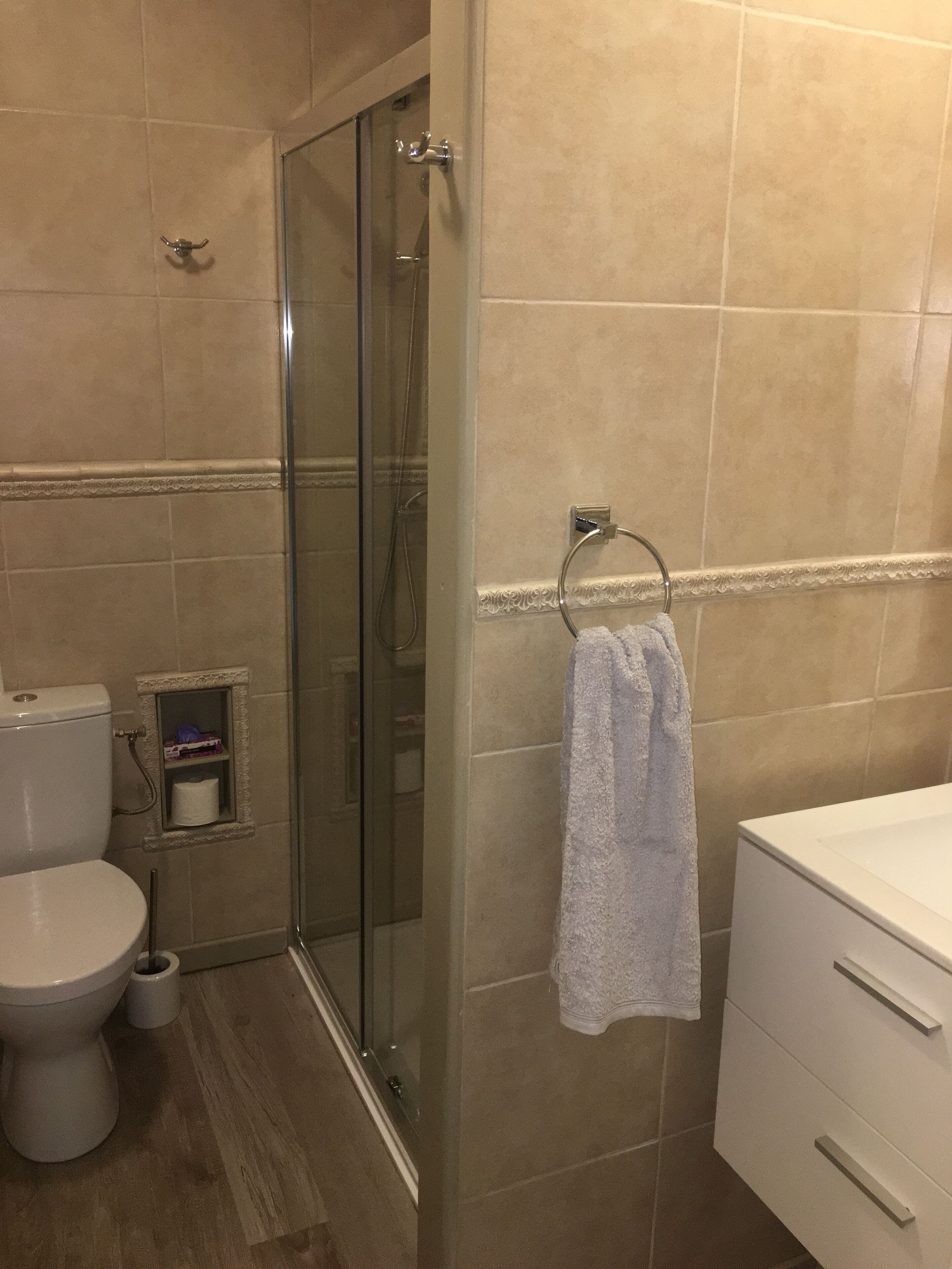 Un baño con cabina de ducha de vidrio, inodoro, lavamanos y perchero para toallas.