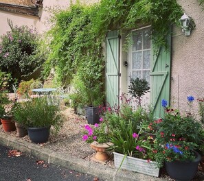 Ein charmantes Gebäude mit einer grünen Tür und einem Fenster, umgeben von Blumentöpfen und Blumen.