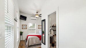 Een slaapkamer met een bed, een plafondventilator, een televisie en een raam met jaloezieën.