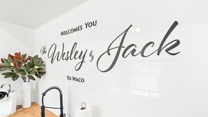 Een keuken met een spoelbak, een plant en een bord aan de muur met de tekst 'WELCOME TO WESLEY & JACK TO WACO'.