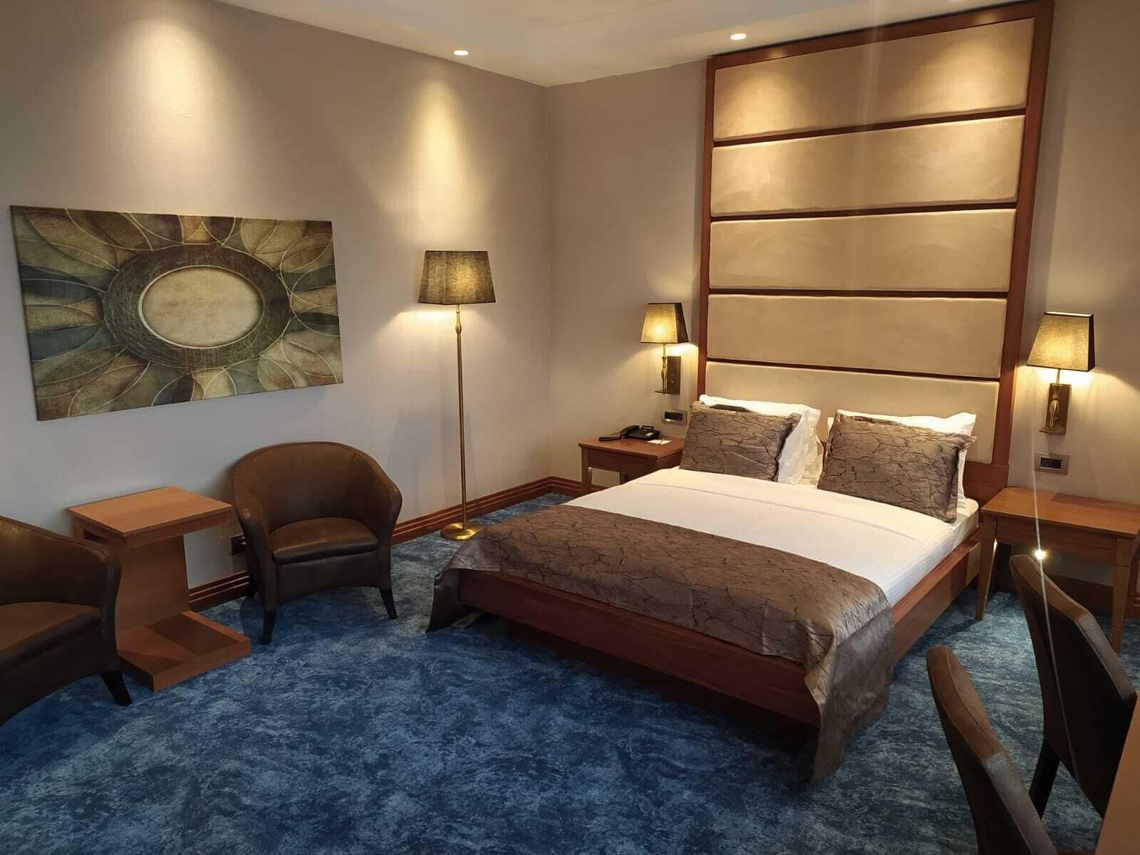 Habitación de hotel con una cama grande, dos mesitas de noche, un escritorio, una silla y una obra de arte colgada en la pared.