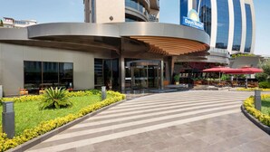 A hotel entrance with a curved facade, a Days Hotel sign, and a landscaped area with yellow flowers and a palm tree.