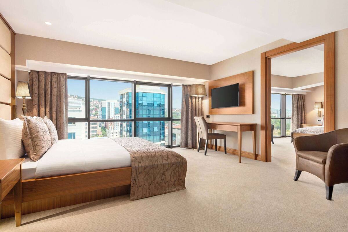 Une chambre d’hôtel avec un grand lit, un bureau, une chaise, une télévision et une vue sur le paysage urbain.