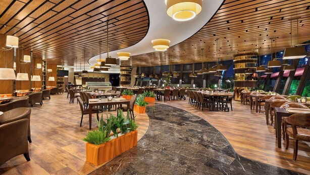 A spacious restaurant with wooden ceiling panels, marble flooring, and multiple seating areas.