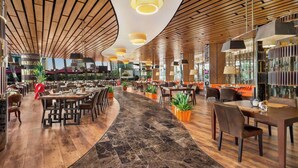 Een ruim restaurant met houten plafondpanelen, marmeren vloeren en moderne verlichtingsarmaturen.