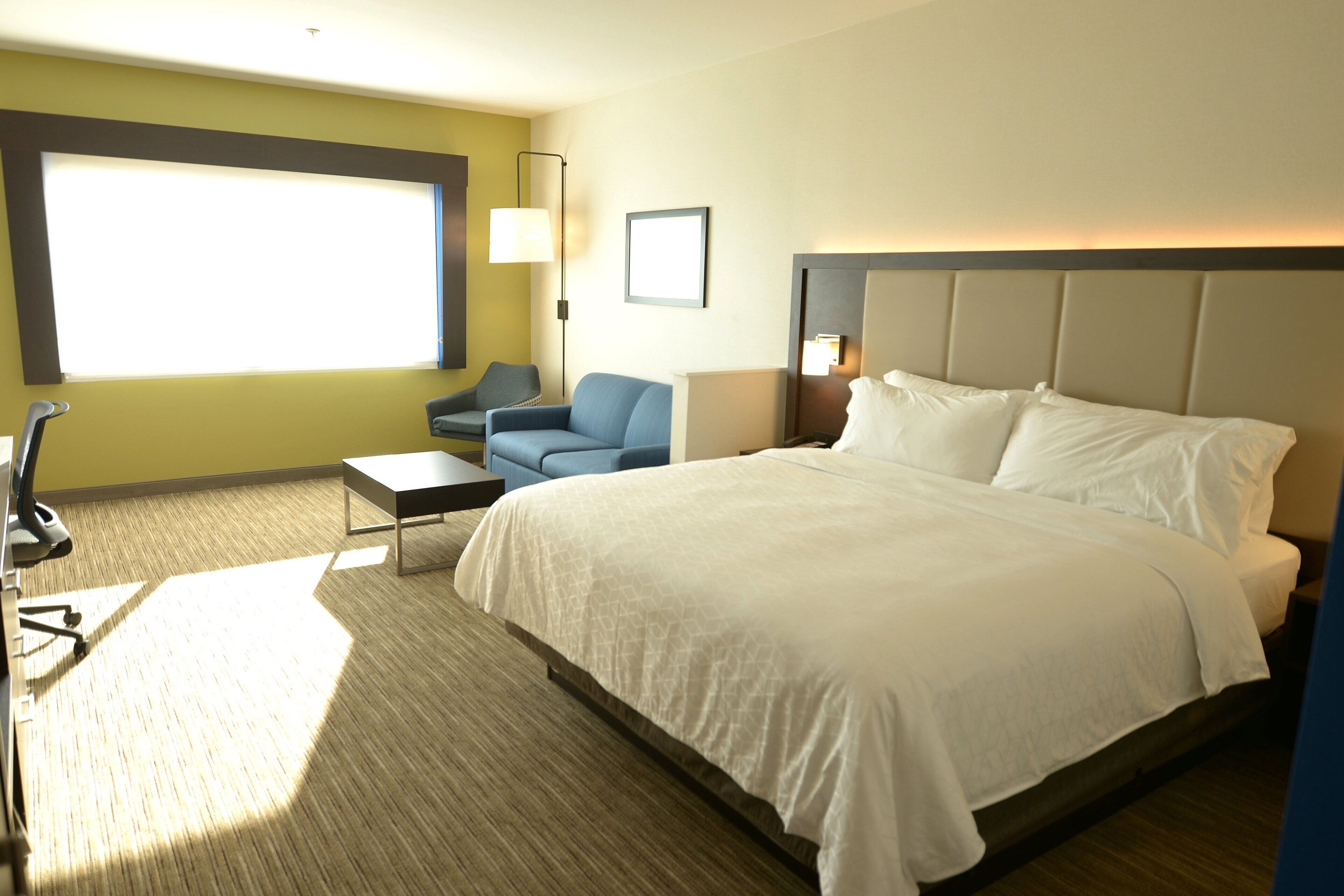 A hotel room with a large bed, a desk, a chair, a lamp, and a window.
