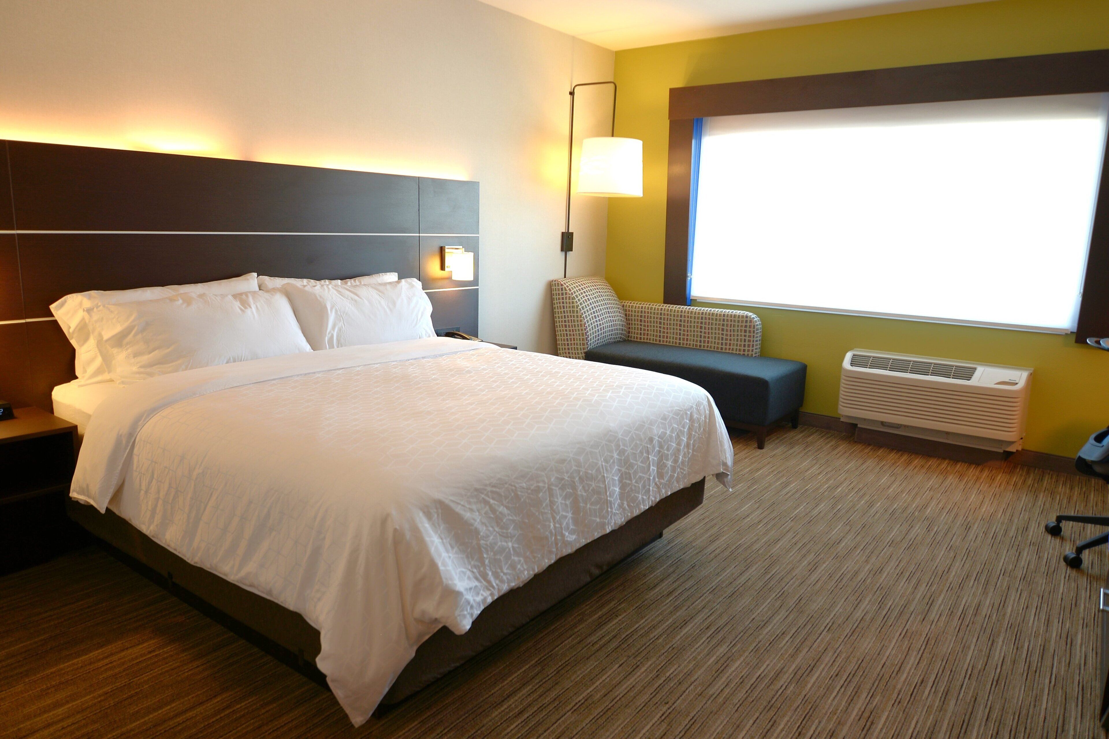 A hotel room with a large bed, bedside lamps, a small seating area, and a window with a view.
