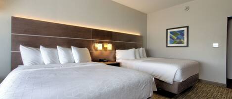 A hotel room with two beds, a headboard with integrated lighting, a bedside table, and a framed picture on the wall.