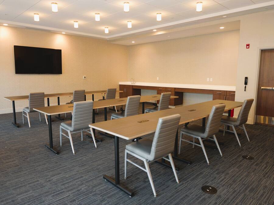 A conference room with multiple tables and chairs, a flat-screen TV mounted on the wall, and a door with a window.