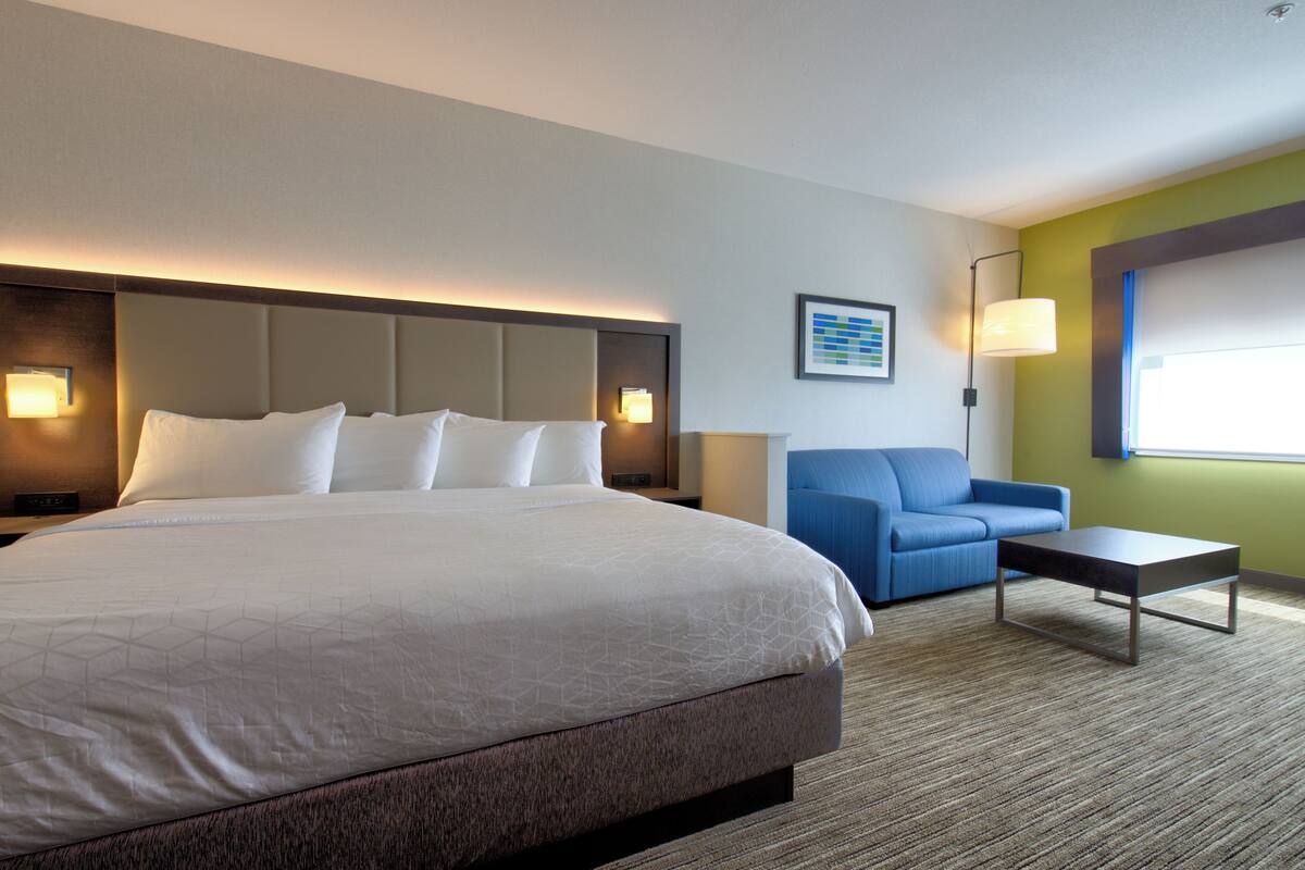 Una camera d'albergo con un letto grande, un divano blu, un tavolino e una lampada.