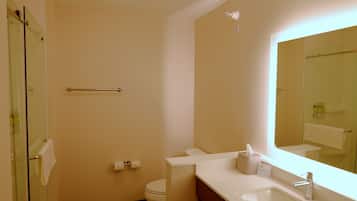 Une salle de bain avec une douche à parois de verre, des toilettes, un lavabo avec un miroir et un porte-serviettes.