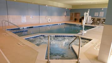 A pool area with a hot tub, lounge chairs, and safety signs.