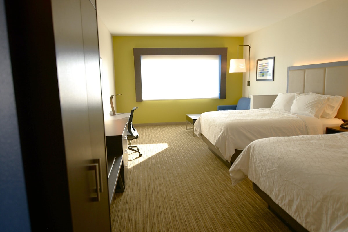 Ein Hotelzimmer mit zwei Betten, einem Schreibtisch mit Stuhl, einem Fenster und einer Lampe.
