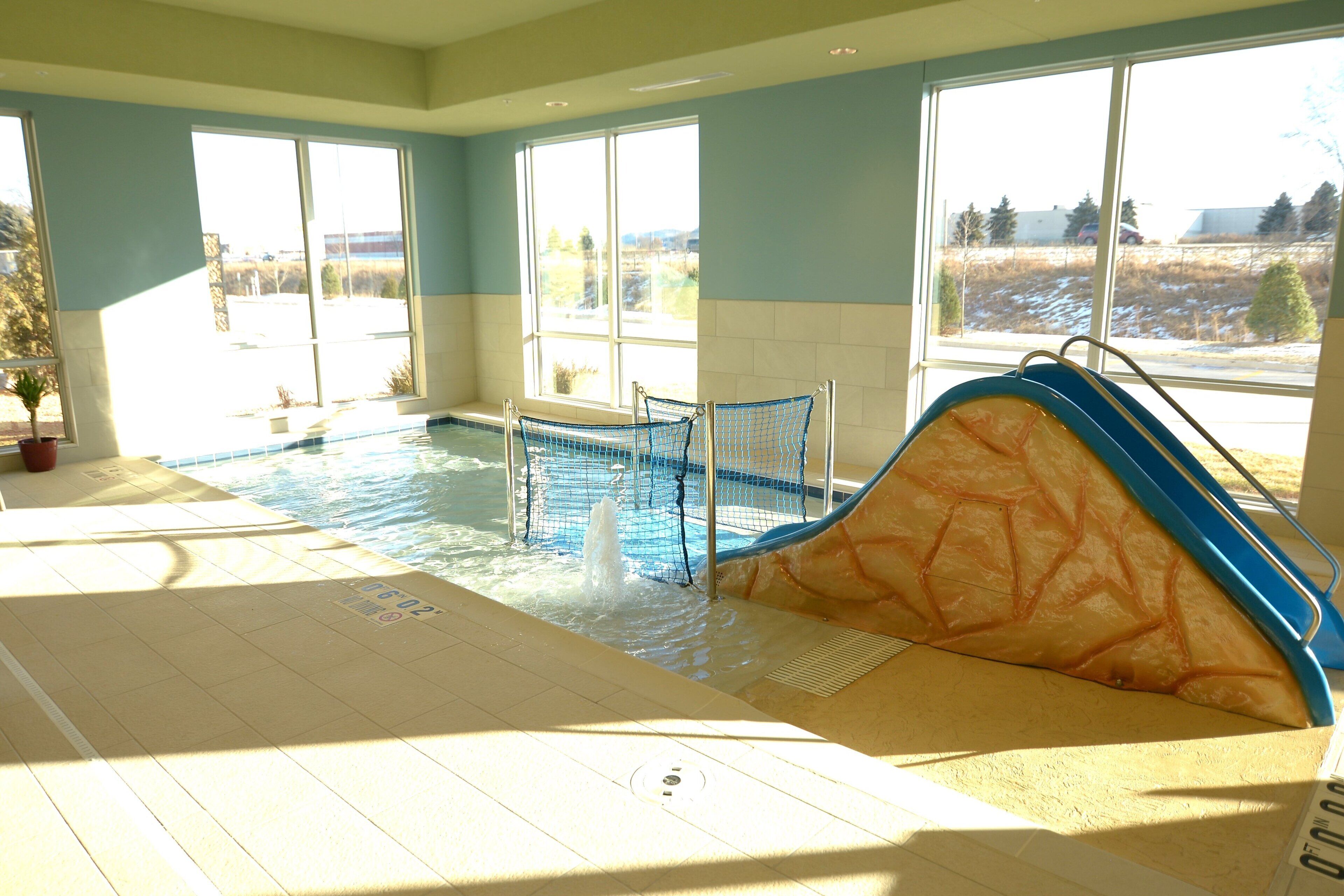 An indoor swimming pool with a slide, large windows, and a view of the outdoors.