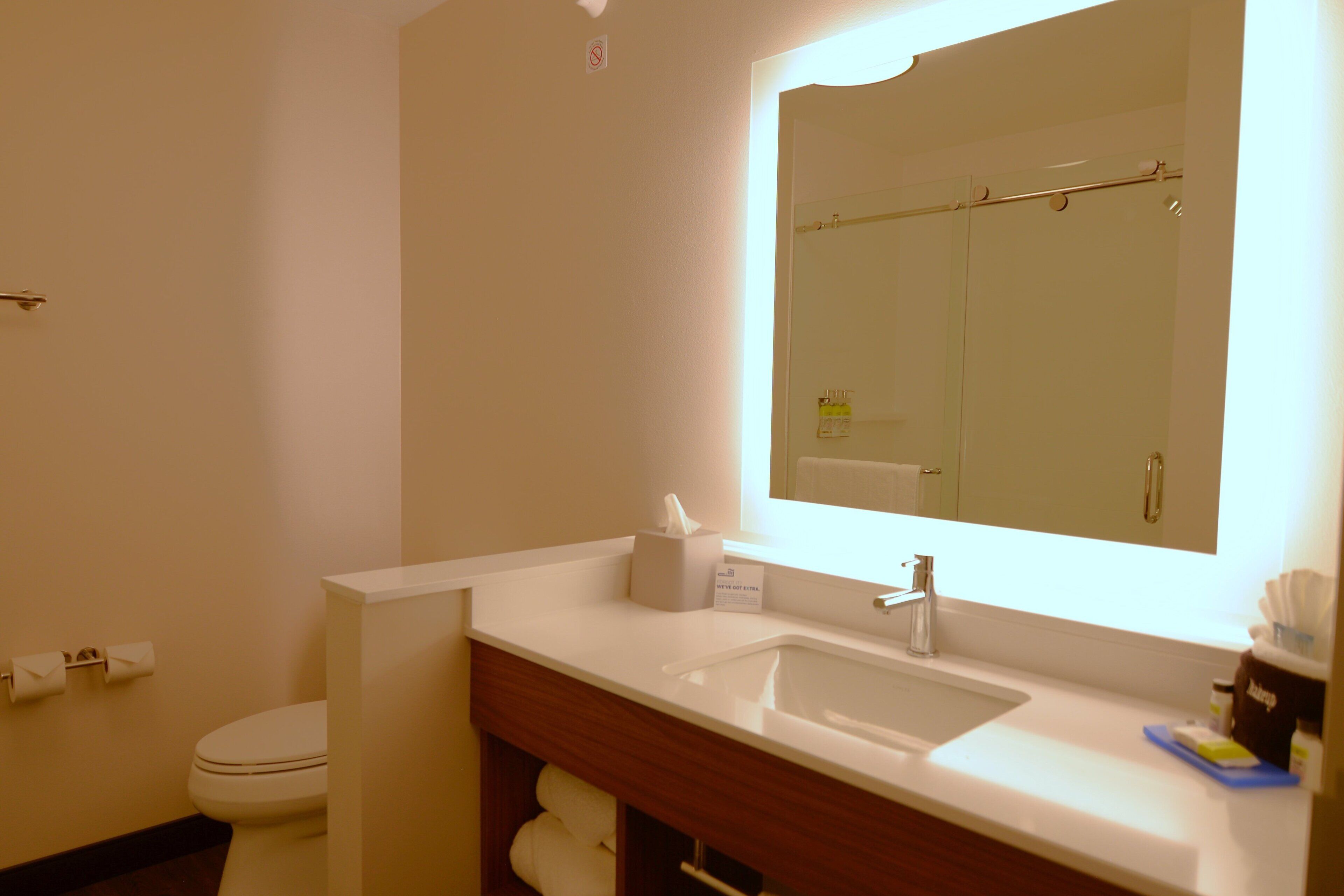 Un baño de hotel con lavabo, espejo, inodoro y toallero.