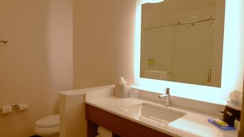 Un baño de hotel con lavabo, espejo, inodoro y toallero.