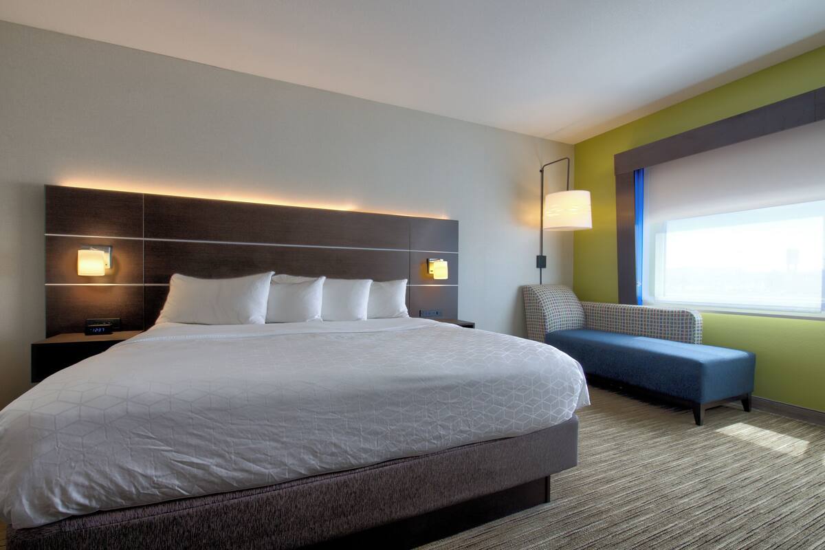 Una camera d'albergo moderna con un letto grande, un comodino, una lampada a parete, un divano e una finestra con tende.