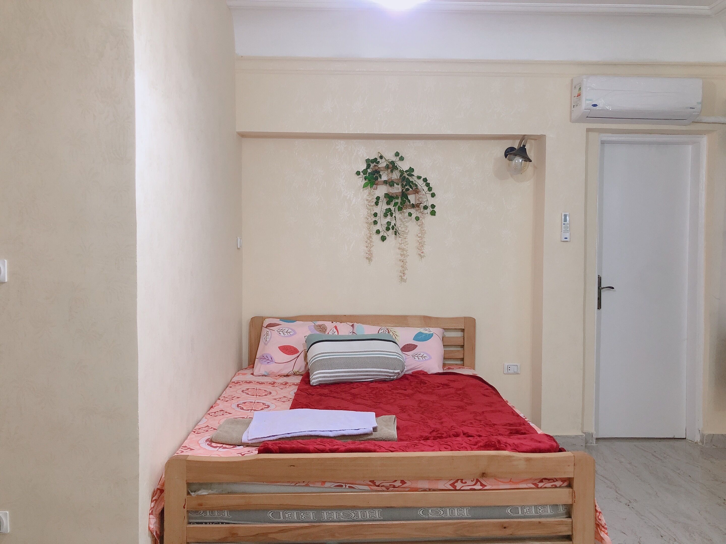 A bedroom with a wooden bed, a red blanket, and a wall-mounted air conditioner.