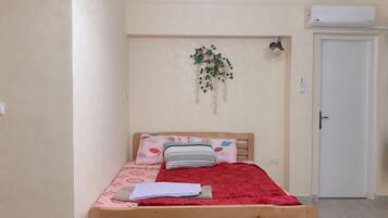 Une chambre à coucher avec un lit en bois, une couverture rouge et un climatiseur fixé au mur.