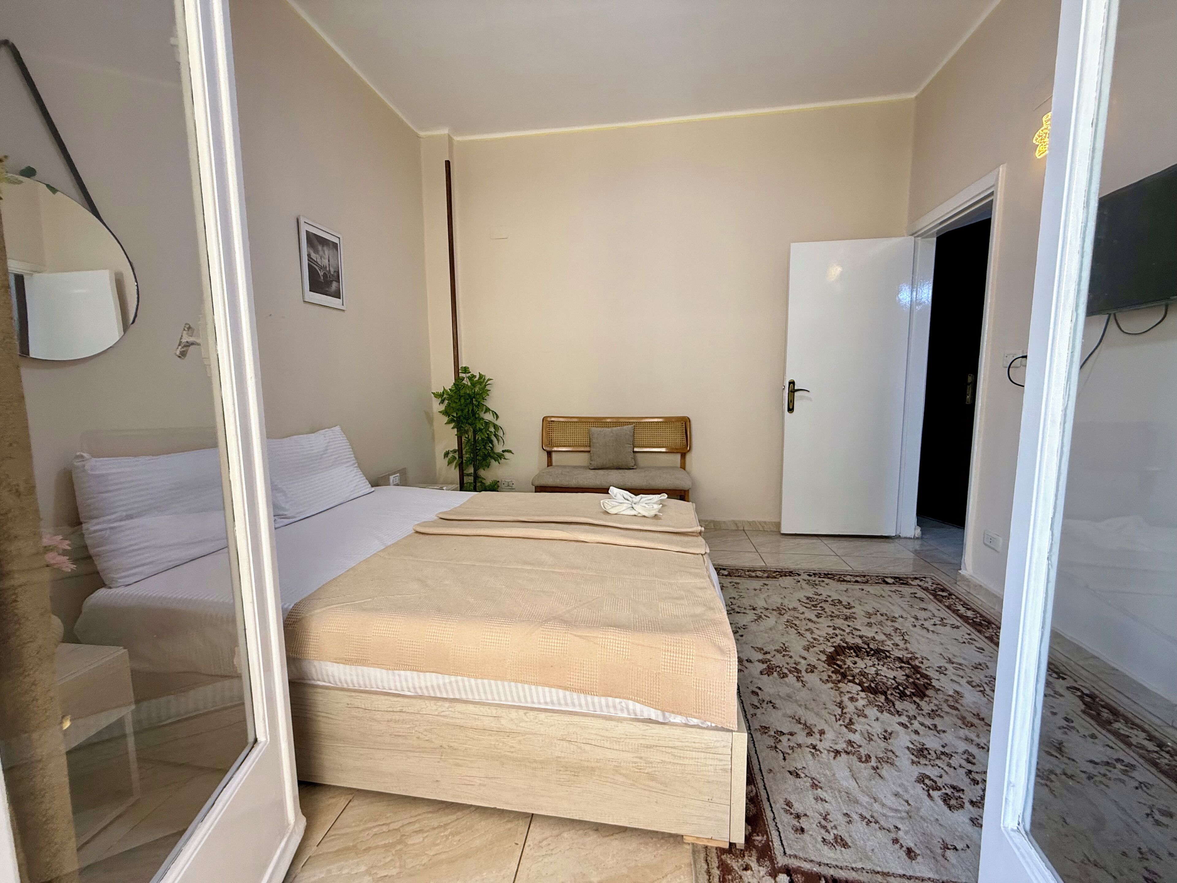 Habitación de hotel con una cama grande, una mesita de noche, una silla, una planta pequeña y una puerta que da a otra habitación.