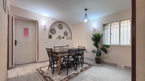 A dining area with a round table, chairs, a rug, a potted plant, decorative wall plates, and a window with curtains. - Downtown Cairo Sweet Home (Cairo)