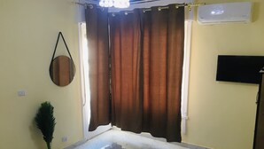 A room with a white marble floor, a potted plant, a pink rug, a curtain, a mounted TV, and a ceiling light fixture. - Downtown Cairo Sweet Home (Cairo)