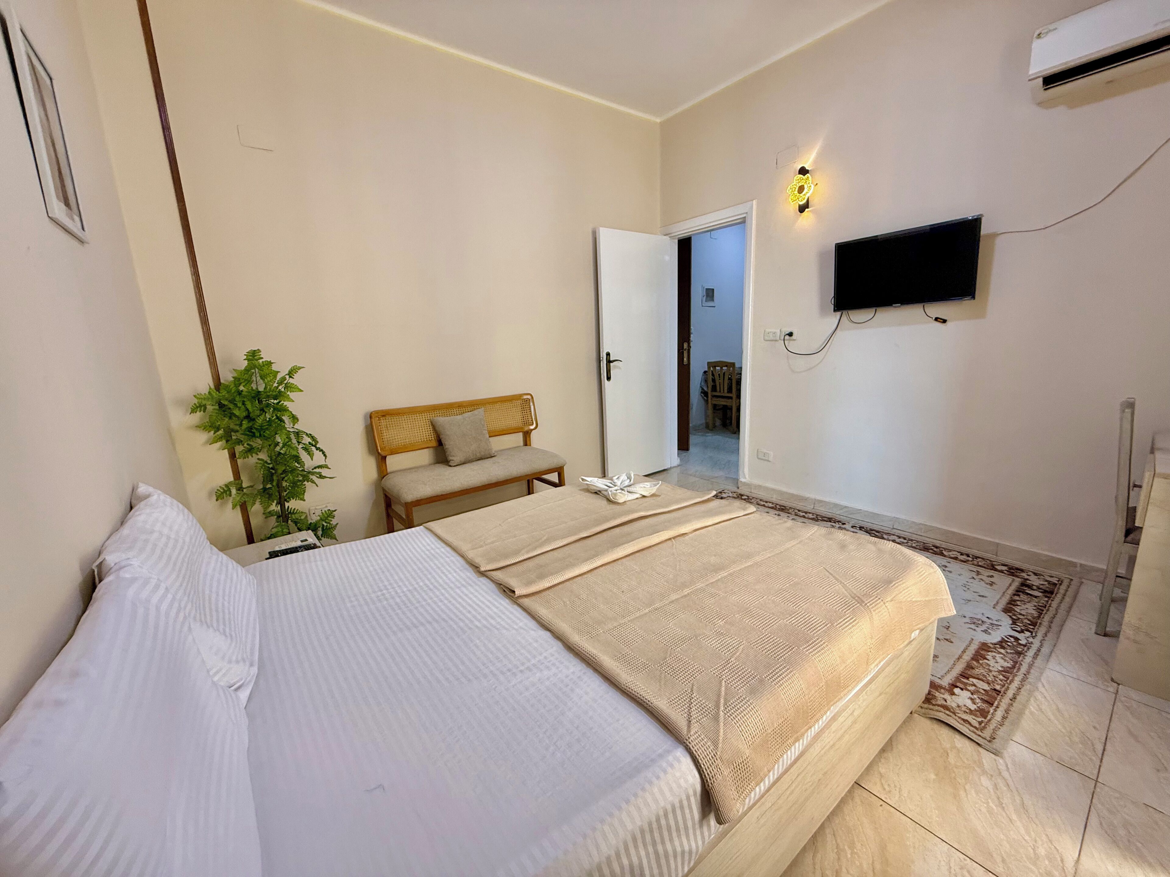 A bedroom with a bed, a bench, a wall-mounted TV, and an air conditioning unit.