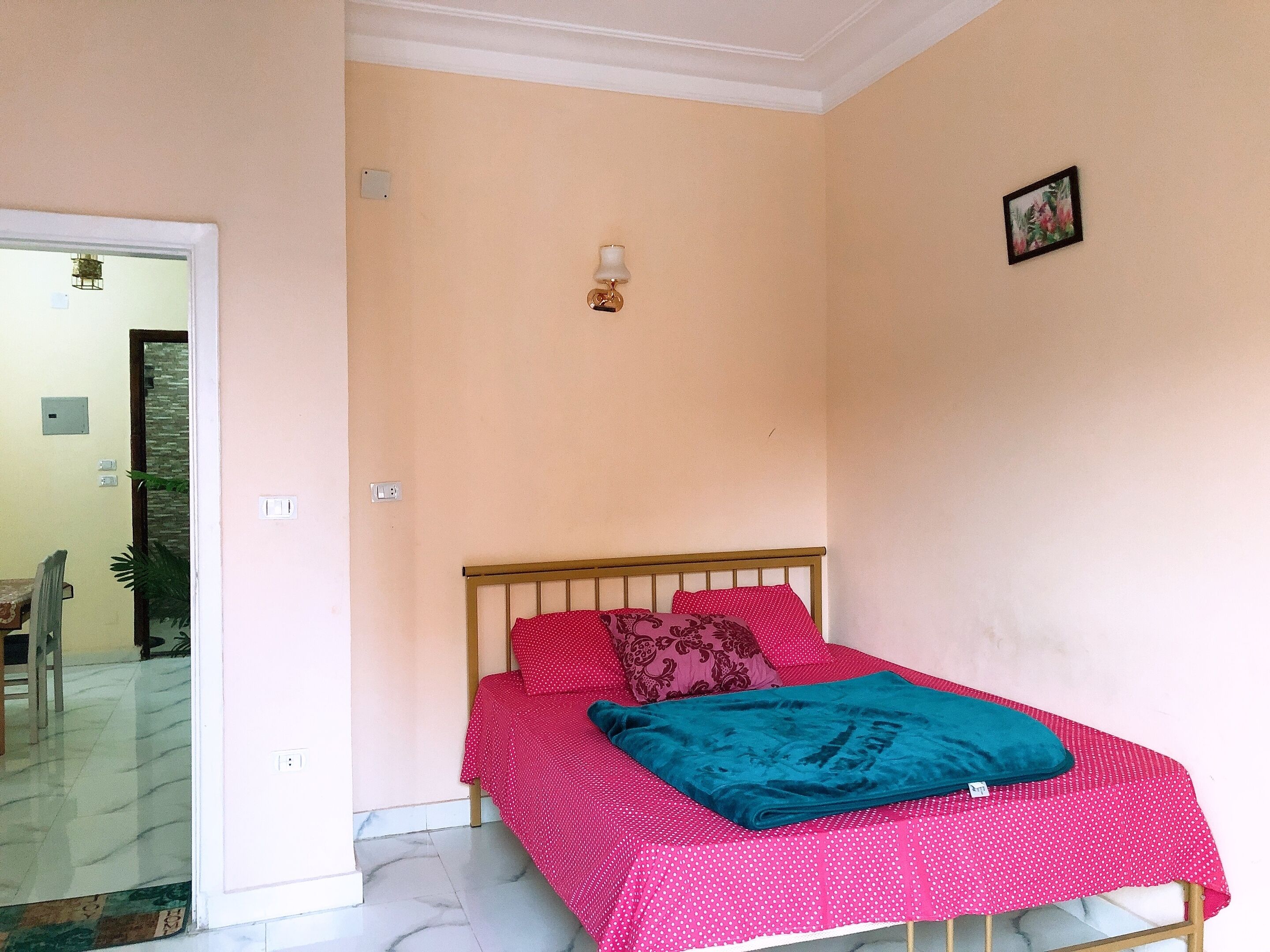 A bedroom with a bed, a nightstand, a wall-mounted lamp, and a small picture.