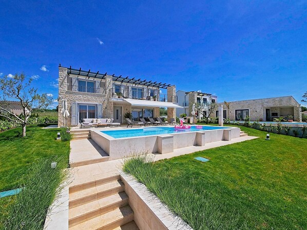 A modern house with a swimming pool, outdoor seating, and a well-maintained lawn.
