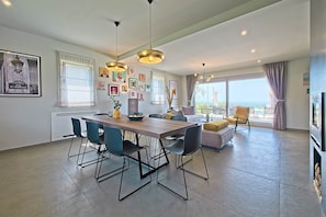 A modern living space with a dining area, a sofa, a TV, and a balcony with a view.