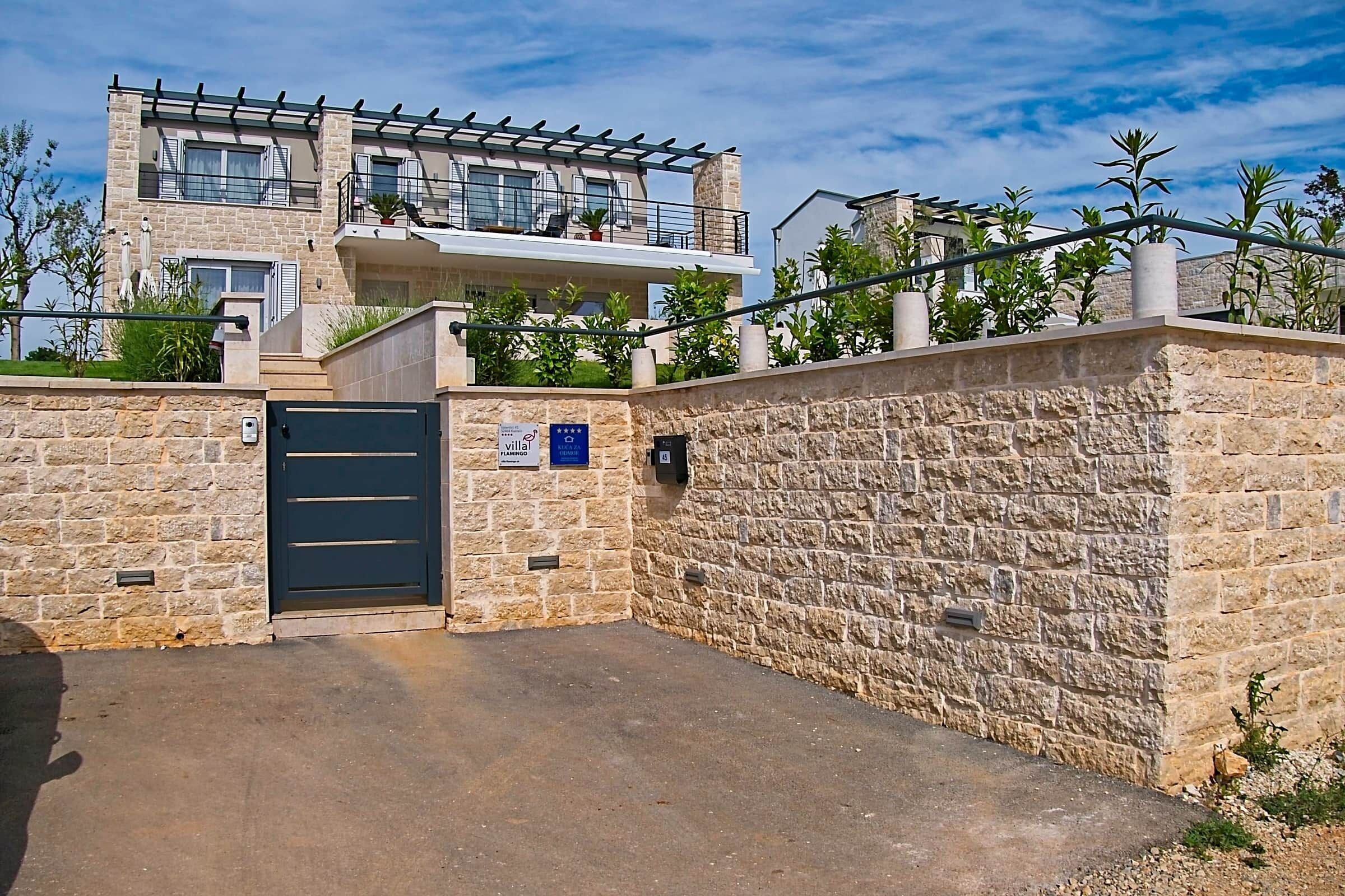 A two-story building with a stone facade, a gated entrance, and a balcony with outdoor seating.