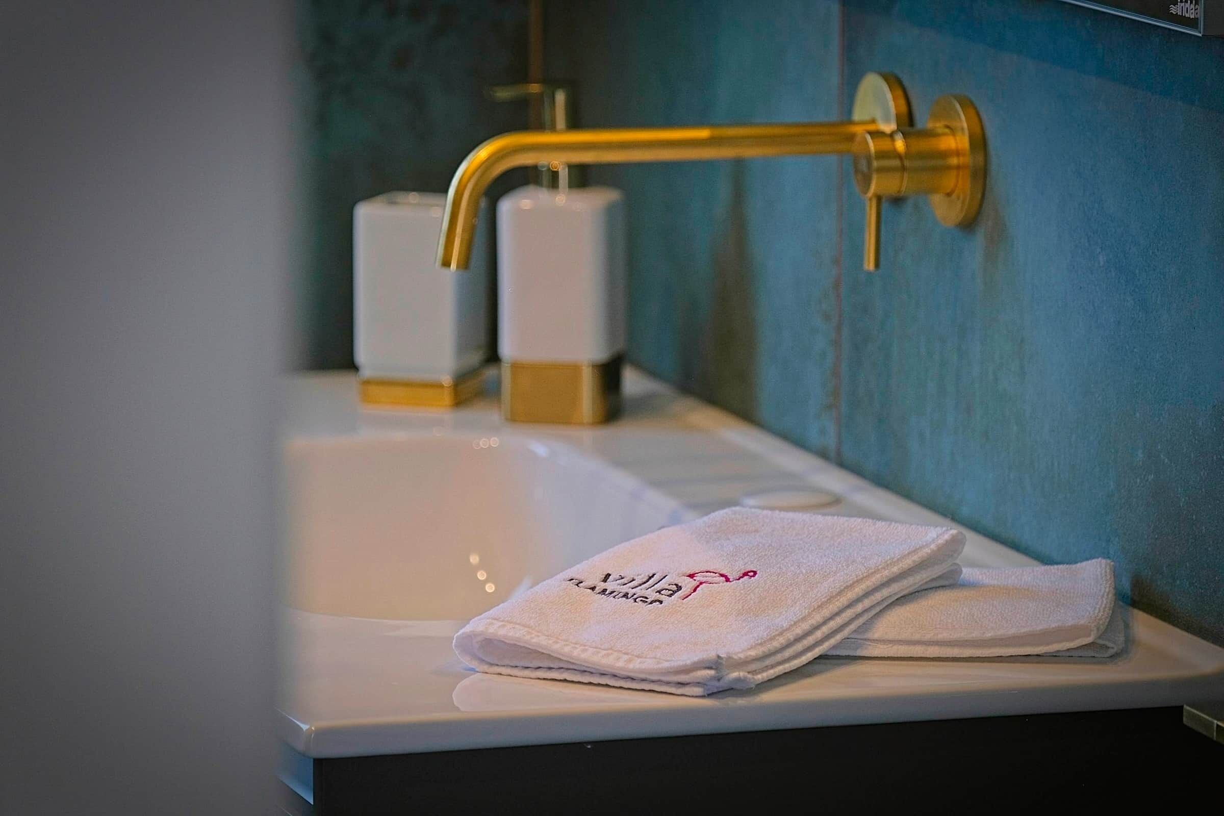 A bathroom with a white sink, gold faucet, and a towel with 'Villa Flamingo' text.