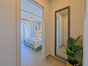 A hotel room with a large bed, a mirror, a potted plant, and a view of the outside.