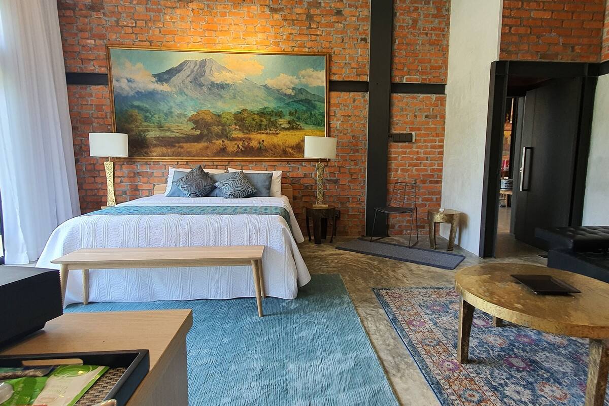 Een hotelkamer met een groot bed, een bankje, een sofa, een kleine tafel en een schilderij aan de muur.