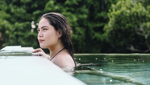 A person leaning on a pool edge with a blurred natural background.