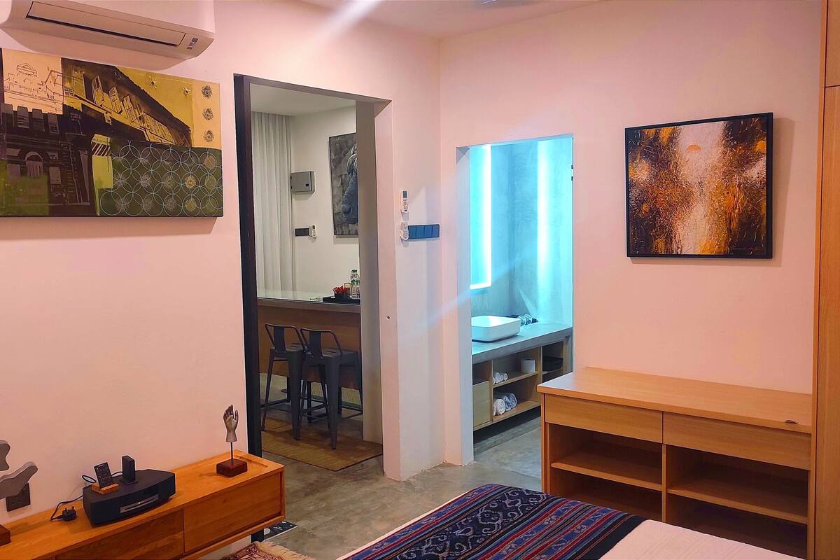 Een hotelkamer met een bed, een bureau met een computer, een stoel en een badkamer door een open deur zichtbaar.