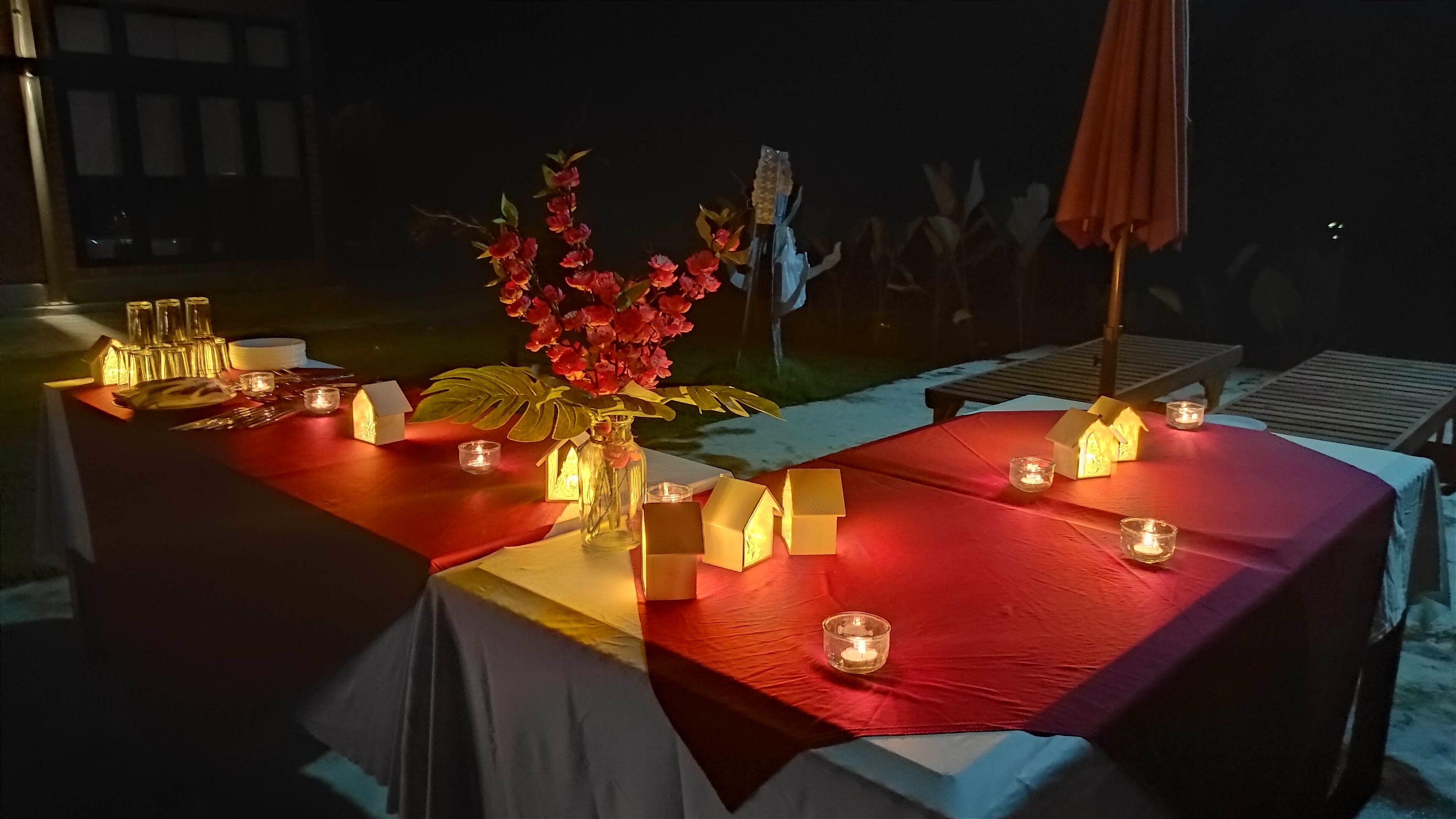 A table set with candles, house-shaped candles, and a vase with flowers.