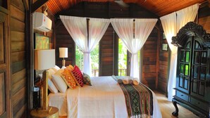 A log cabin bedroom with a bed, a nightstand, a lamp, a wardrobe, and sheer curtains.