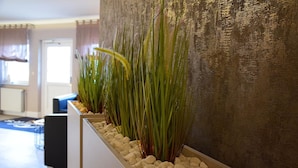 A modern interior with a long planter box containing tall green plants and white pebbles, a blue sofa, and a textured wall.