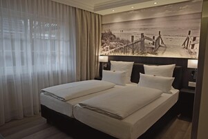 Ein Doppelbett mit weißen Bettwäsche, ein Kopfteil mit einem Strandbild und ein Nachttisch mit einer Lampe.