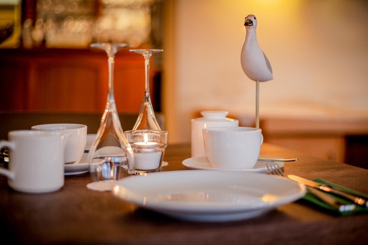 Un tavolo da pranzo con tazze bianche, un decanter di vetro, una candela e una statuetta di uccello decorativa.