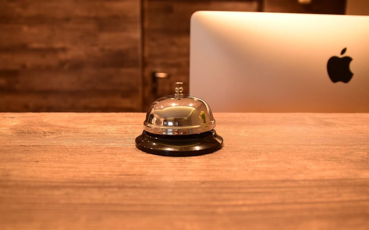 A wooden table with a clear glass bell and a laptop with an Apple logo.