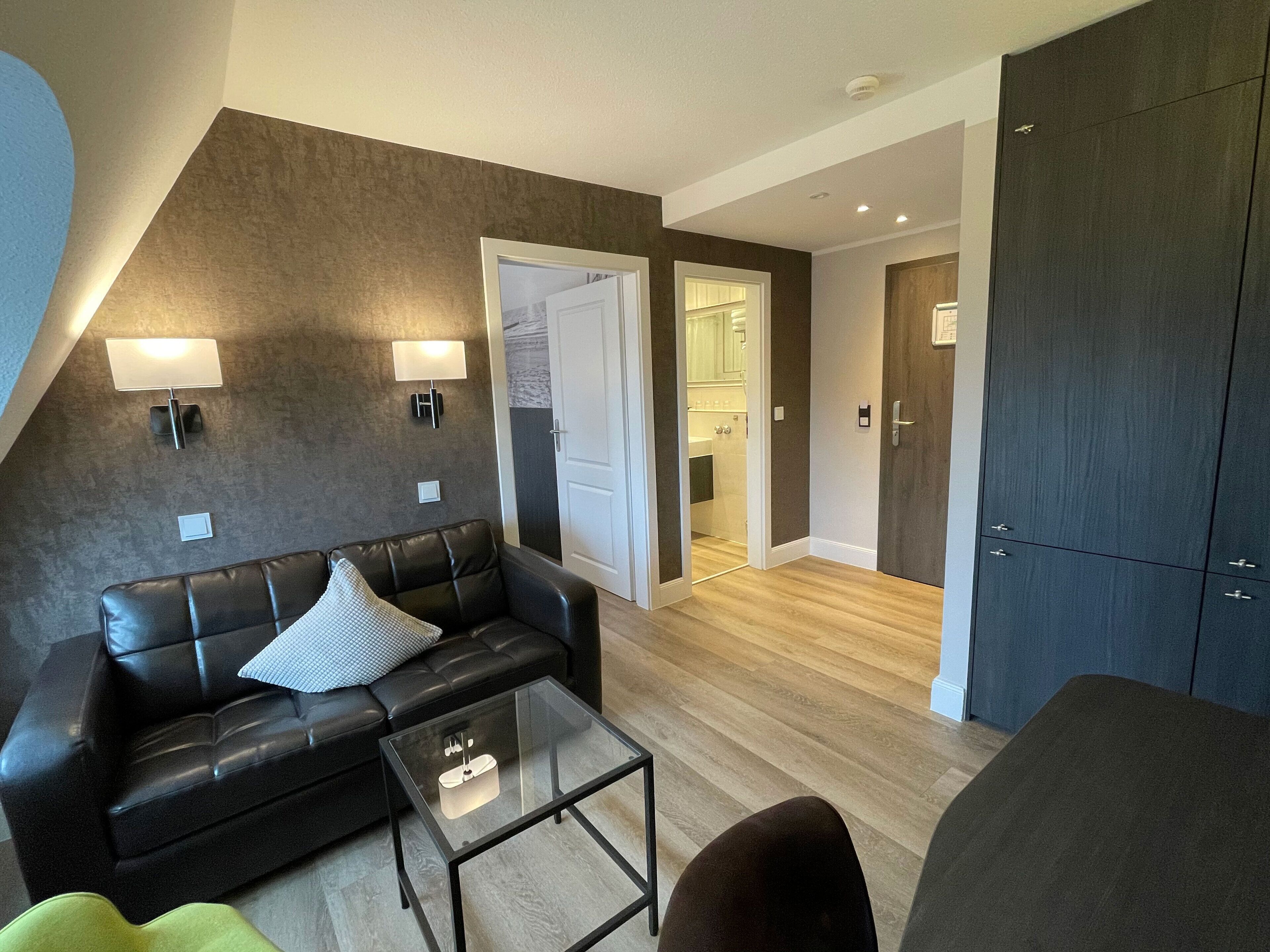 A modern living room with a leather sofa, a glass coffee table, and a dark wardrobe.