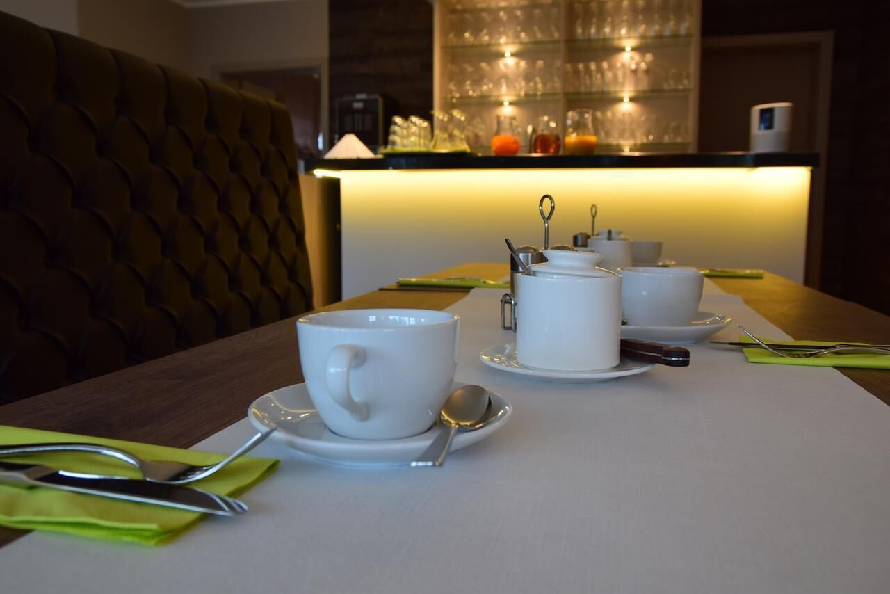 A dining table set with white cups and saucers, a spoon, and a knife on a white placemat.