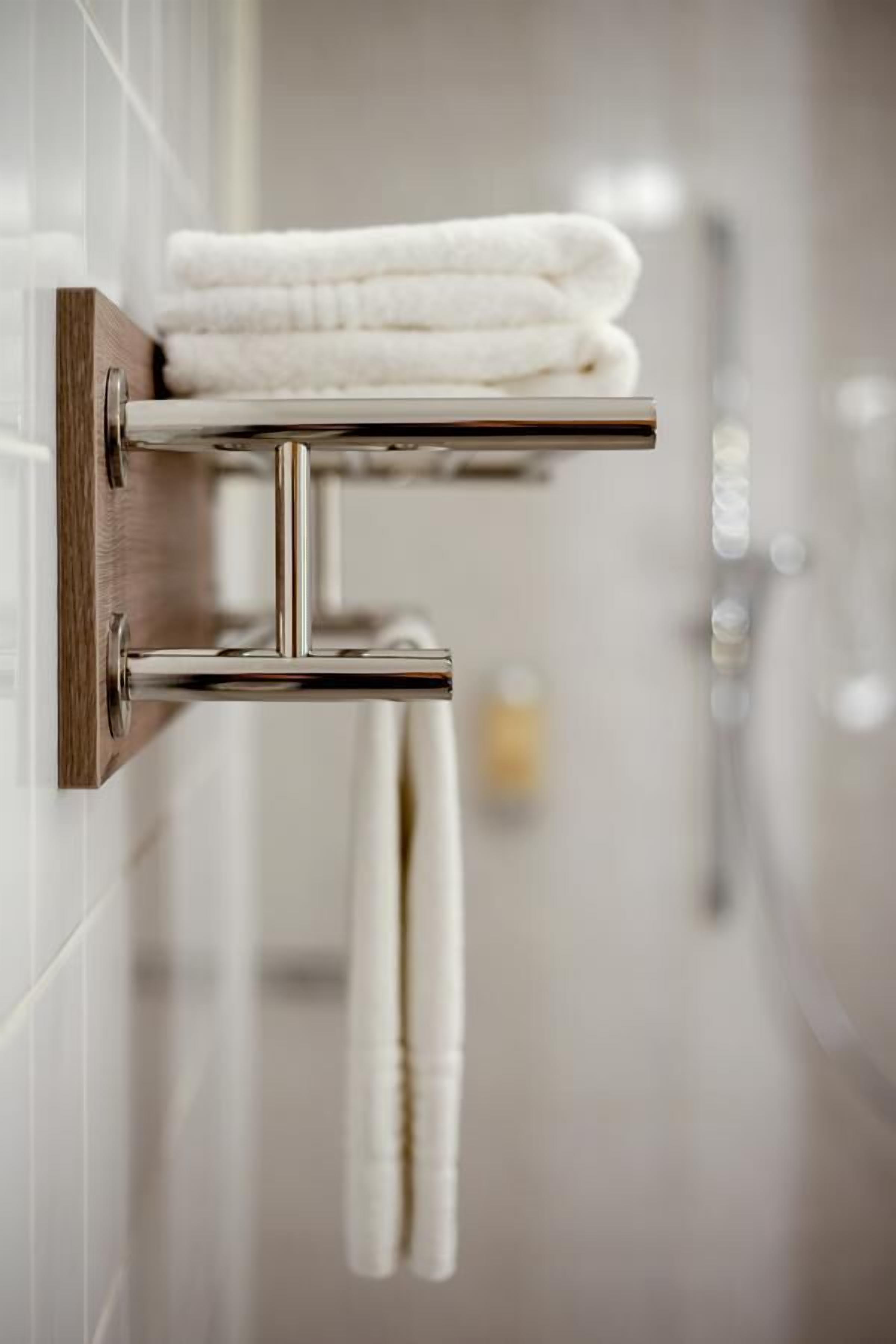 Een badkamer met een handdoekrek vol opgevouwen handdoeken, een douche en een glas water op de wastafel.